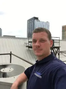 A man standing on top of a building next to a fan.